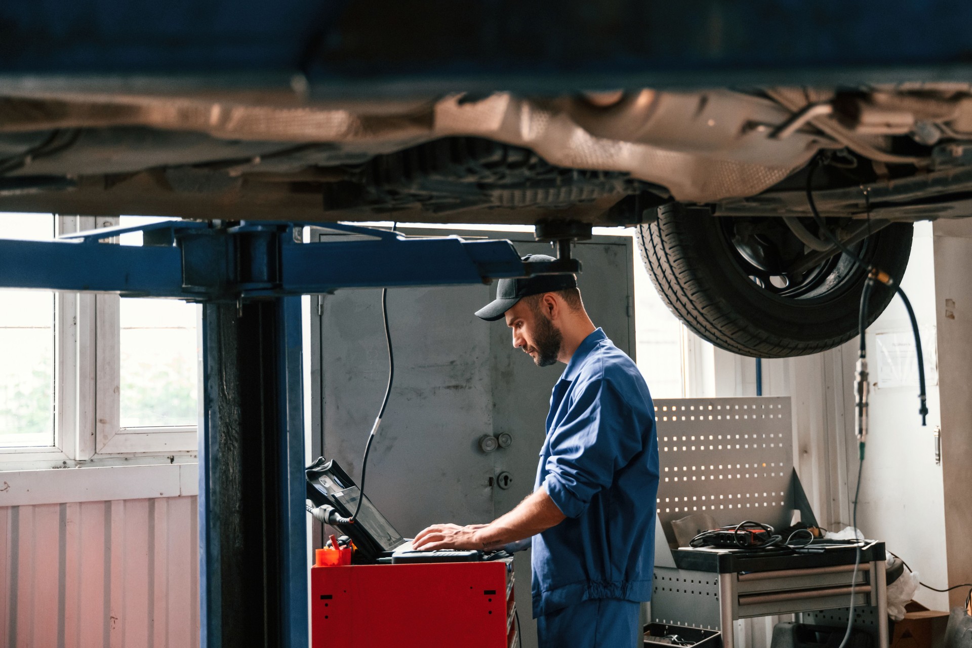 Using laptop and testing device. Auto mechanic working in garage. Repair service